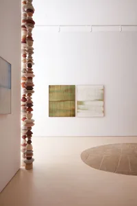 A minimalist gallery space featuring modern abstract art on the walls and a sculpture made of stacked stones.