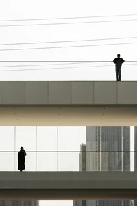 A modern glass bridge features architectural designs with urban infrastructure visible in the background.