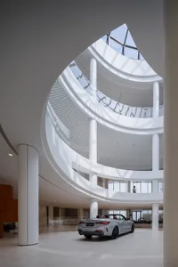 A sleek, modern car dealership interior with a spiraling staircase and white, glass walls.