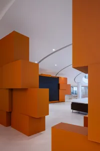 A modern office space featuring orange cube structures, white walls, and a concrete floor.