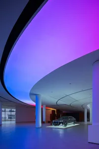 A sleek, modern car showroom with glass walls and a curved, illuminated ceiling.