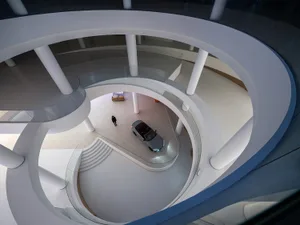 A modern white circular spiral staircase with glass railings and a white concrete structure.