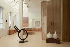 A modern art gallery featuring a minimalist interior in neutral tones, with various artworks and sculptures displayed.
