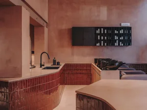 A modern hair salon featuring red tile and concrete surfaces with a color bar and wash stations.