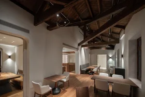 Interior view of an industrial-style restaurant dining room with wooden tables and chairs, featuring exposed wooden beams and