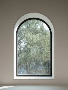 An arched window framed in glass with a view of lush green trees outside.