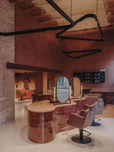 A minimalist salon interior with concrete flooring, tile accents, and modern lighting fixtures.
