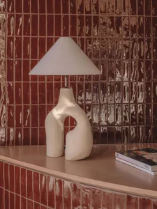 A modern, abstract ceramic lamp with a conical shade in a living room setting.