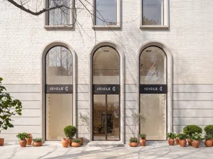 Modern retail storefront with glass windows, concrete accents, and potted plants outside the entrance.