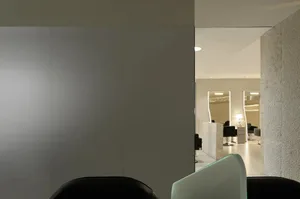 A modern salon interior with sleek white walls, black chairs, and a view into the reception area with white stone walls and i