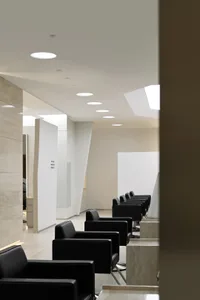 Modern salon with black leather seating, marble countertops, and glass paneling.