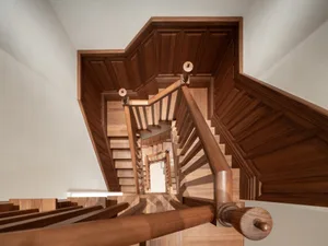 Modern wood staircase with brown wooden railing and steps, viewed from above.