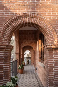 A brick walkway with archways leading to a door with a window and green potted plants.