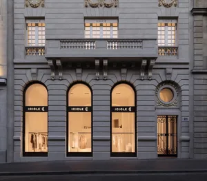 An elegant, stone storefront with arched windows displaying clothing.