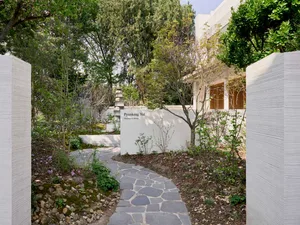 A modern garden featuring natural stones surrounded by concrete pathways and walls, surrounded by greenery and trees.