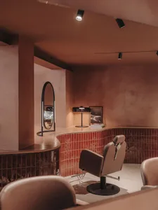 An interior photograph of a modern hair salon featuring a hair styling chair and red-tile accents.