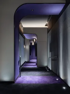 An interior photograph of a modern hotel corridor featuring minimalist design elements such as vinyl flooring and concrete co