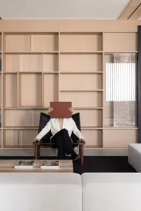 A modern, minimalist living room with a white sofa, black coffee table, and wooden shelving unit.