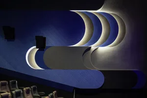 Modern cinema theater interior with metallic textured screens and curved lighting fixtures.