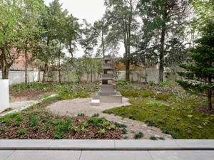 A contemporary garden with moss, trees, and a minimalist sculpture on a gravel path.