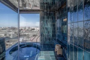 An outdoor modern bathroom with a blue tiled hot tub overlooking a scenic landscape.
