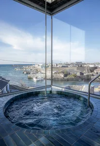 A hot tub set against a stunning coastal view, with water flowing and a clear blue sky above.