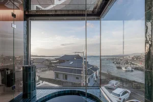 A minimalist window view of a coastal town with glass siding and blue-tiled floor.