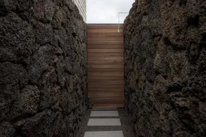 A modern doorway constructed from wooden panels, bordered by dark stone walls.