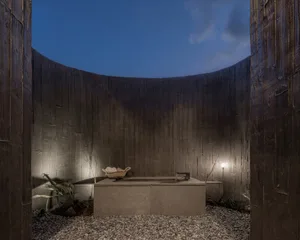 A minimalist bathroom with concrete walls, a stone floor, and a simple vanity and sink.