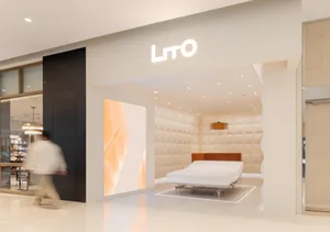 A modern bedroom showcasing a brown upholstered bed against a soft-textured fabric wall, illuminated by ceiling lights, with 