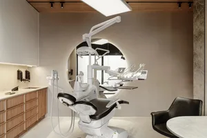 A minimalist dental office with a white dental chair and wooden cabinets.