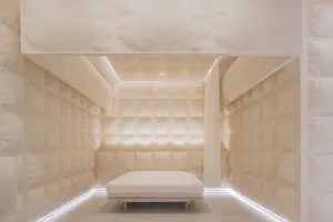 A minimalist bedroom with fabric walls, a single white mattress on a wooden platform, and ambient lighting.