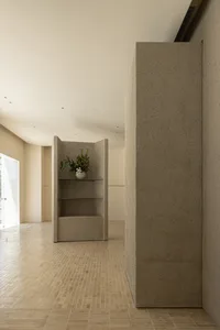 A minimalist room with concrete walls and floors, featuring a vase of flowers on a shelf.