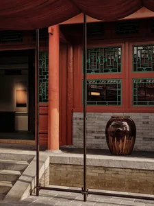 A traditional building exterior with a red wooden column, green-mesh windows, and a large brown vase.