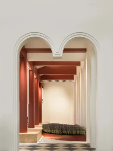 A modern interior corridor with concrete walls, terracotta arches, and a checkered floor.
