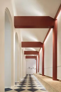 A minimalist corridor with concrete walls and red structural beams.