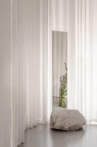 A minimalist interior with neutral materials and a rock-like object in front of sheer curtains.
