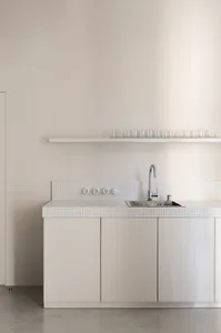 A minimalist kitchen with white ceramic tiles and cabinets.