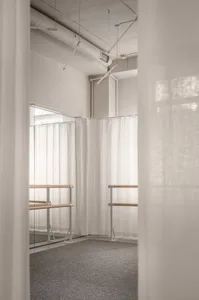 極簡舞蹈工作室，配有白色窗簾與木製芭蕾扶手。