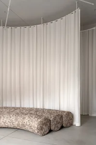 A minimalist sofa upholstered in a printed fabric design, placed against a backdrop of white curtains.