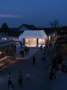 A modern cultural center with a glass facade and open interior space illuminated by warm lighting.