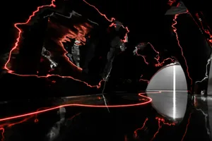 A modern art installation featuring bold, red laser light patterns against a dark background.