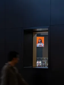 A digital retail display featuring a man with dreadlocks in sunglasses, backlit by an orange background.