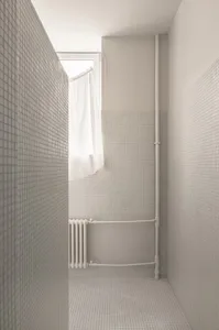 A minimalist bathroom featuring grey tiles and a window with a white curtain.