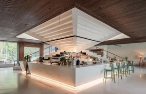 Modern-looking cafe bar with concrete finish, featuring green stools on white rests and a large, open space with a glass wall