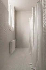 A modern bathroom with white tiled walls and floor, and white curtains.