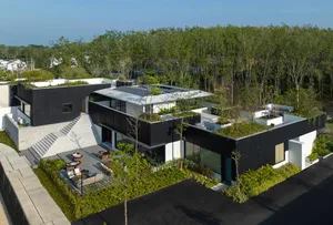 Modern black house with concrete exterior and glass windows surrounded by greenery.