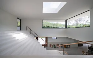 A modern living room with concrete walls and floor, featuring large windows and a skylight.
