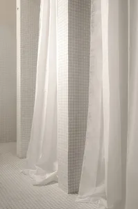 A minimalist public bathroom with white tiles and white fabric dividers.