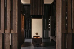 A minimalist interior space featuring a wooden teapot hanging above a wooden bench, with tall wooden panels and shelves.